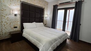Une chambre avec un grand lit, une tête de lit, une table de chevet, une lampe fixée au mur et une vue sur l’extérieur, visible à travers une porte.