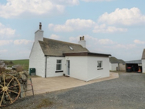 A small white building with a sloped roof and two chimneys, a paved driveway, and a stone wall with a wheelbarrow. - South Kirklauchline Farm (Stranraer)