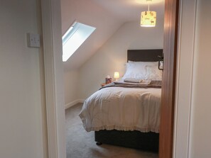 A bedroom with a sloped ceiling, a skylight, a bed with white bedding, a bedside lamp, and a nightstand. - South Kirklauchline Farm (Stranraer)