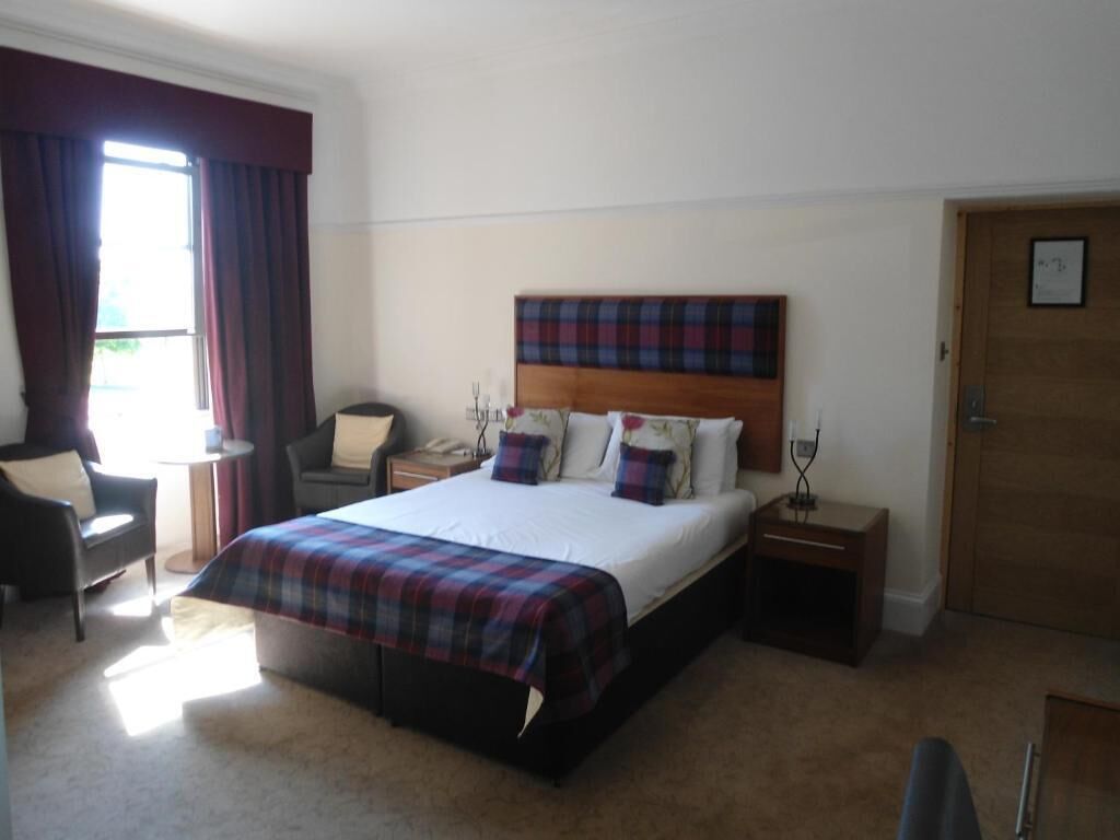 A hotel room with a bed, bedside tables, a chair, a desk, a lamp, and a door.