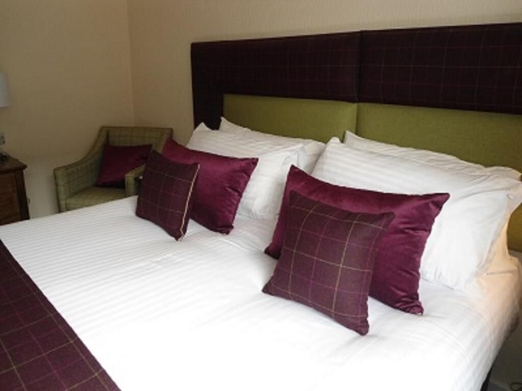 A hotel room with a large bed, green headboard, and multiple pillows.
