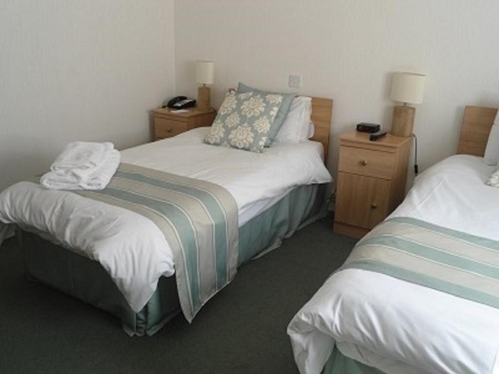 A hotel room with two single beds, bedside tables with lamps, and a small nightstand with a phone.