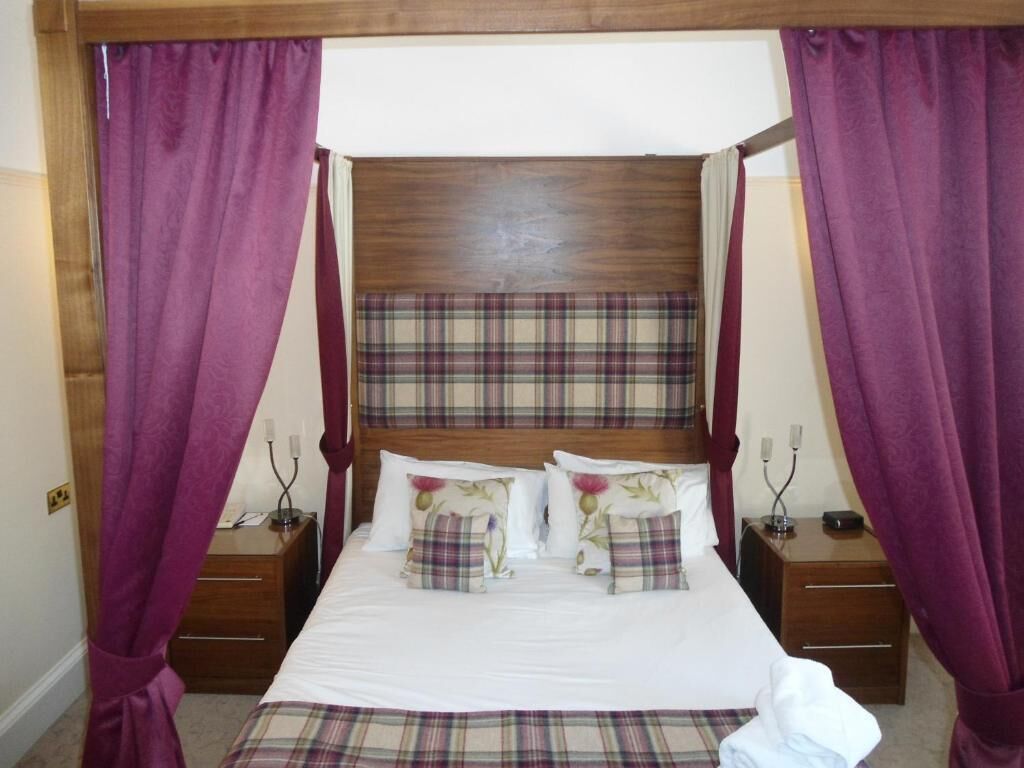 A four-poster bed with a plaid headboard, two bedside tables, and purple curtains.