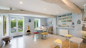 A spacious kitchen with a dining area, large windows, and a rustic ceiling. - Gîte "Gite De La Rampotiere" with Private Terrace, Garden, and Wi-Fi (Quettreville-sur-Sienne)