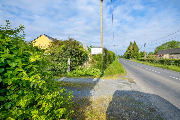 En landevej med en gul bygning til venstre, omgivet af grøn vegetation.