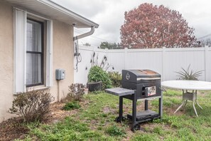 A backyard with a barbecue grill, a window, and a white fence.