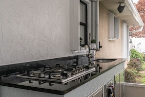 Una cocina con estufa a gas, un lavamanos y una ventana con persianas.