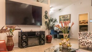 Ein Wohnzimmer mit Flachbildfernseher, Soundsystem, Essbereich und Blumenarrangement.