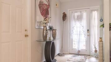 A hallway with a glass console table, a vase with flowers, a sculpture, and a door with curtains.