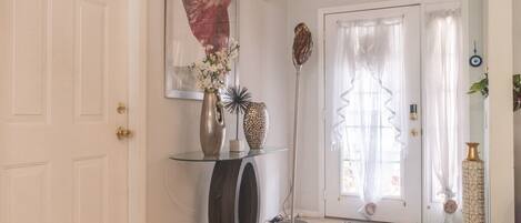 A hallway with a glass console table, a vase with flowers, a sculpture, and a door with curtains.