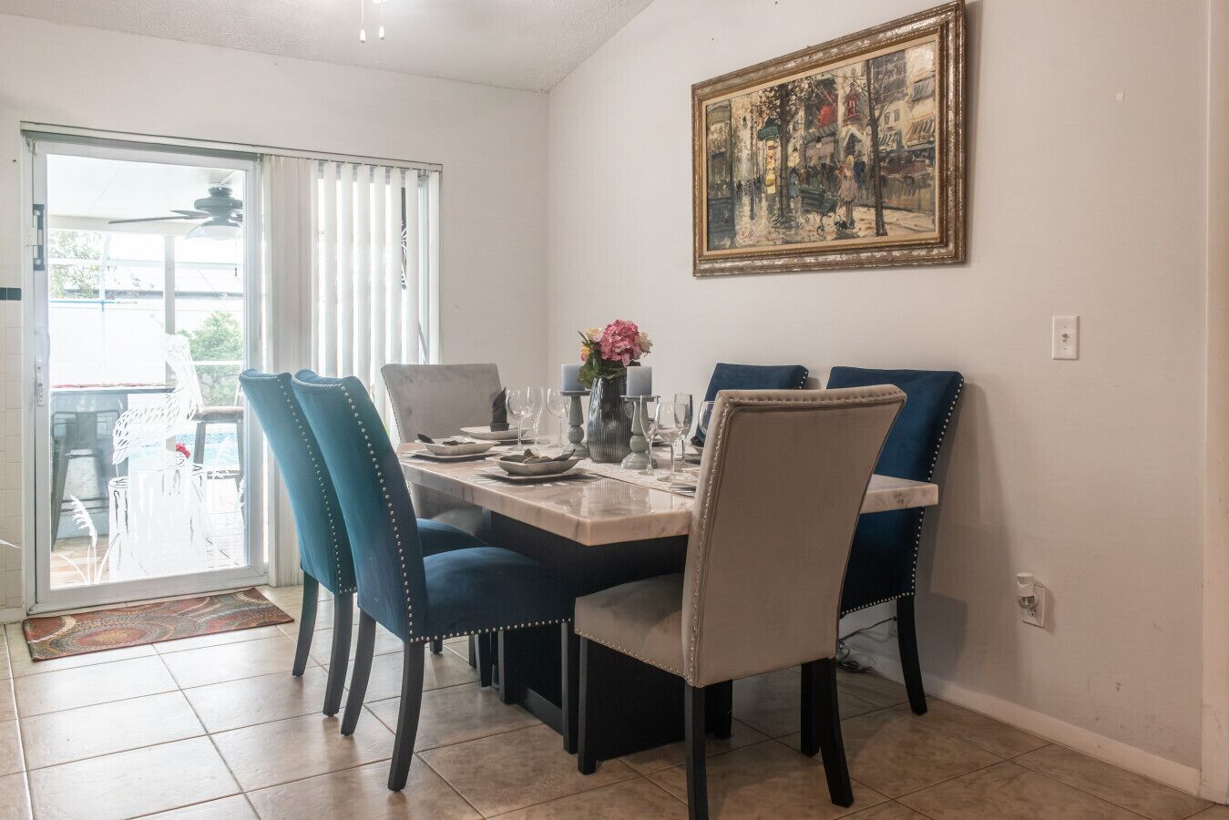 A dining area with a table set for four, blue chairs, a painting on the wall, and a sliding glass door leading outside.
