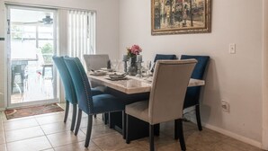 Ein Essbereich mit einem für vier Personen gedeckten Tisch, blauen Stühlen, einem Gemälde an der Wand und einer Glasschiebetür, die nach draußen führt.