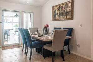 Un comedor con una mesa dispuesta para cuatro, sillas azules, un cuadro en la pared y un ventanal corredero que da al exterior.