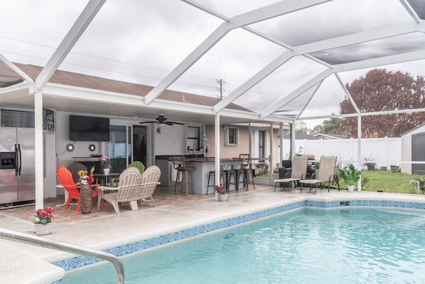 Un espacio al aire libre techado con piscina, mobiliario y una parrilla.
