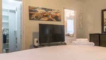 A bedroom with a bed, a flat-screen TV, a painting, a mirror, and a bathroom visible through an open door.