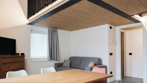 A modern living space with a wooden dining table, a grey sofa, a television, and a window with curtains. - Apartment 2 Casa Bepa - In the heart of Bormio, ideal for skiing and relaxation (Bormio)