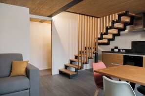 Ein modernes Interieur mit grauem Sofa, einer Holztreppe, einer Küchenzeile und einem Esstisch.