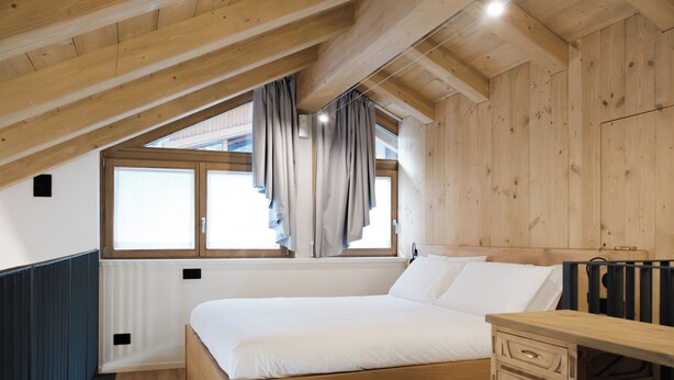 A bedroom with a wooden ceiling, a window with curtains, a bed, a bedside table, and a radiator. - Apartment 2 Casa Bepa - In the heart of Bormio, ideal for skiing and relaxation (Bormio)
