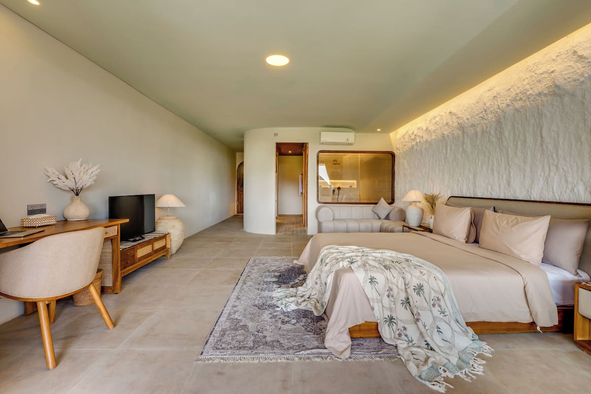 A modern bedroom with a bed, bedside tables, a desk, a chair, a television, and a large mirror.