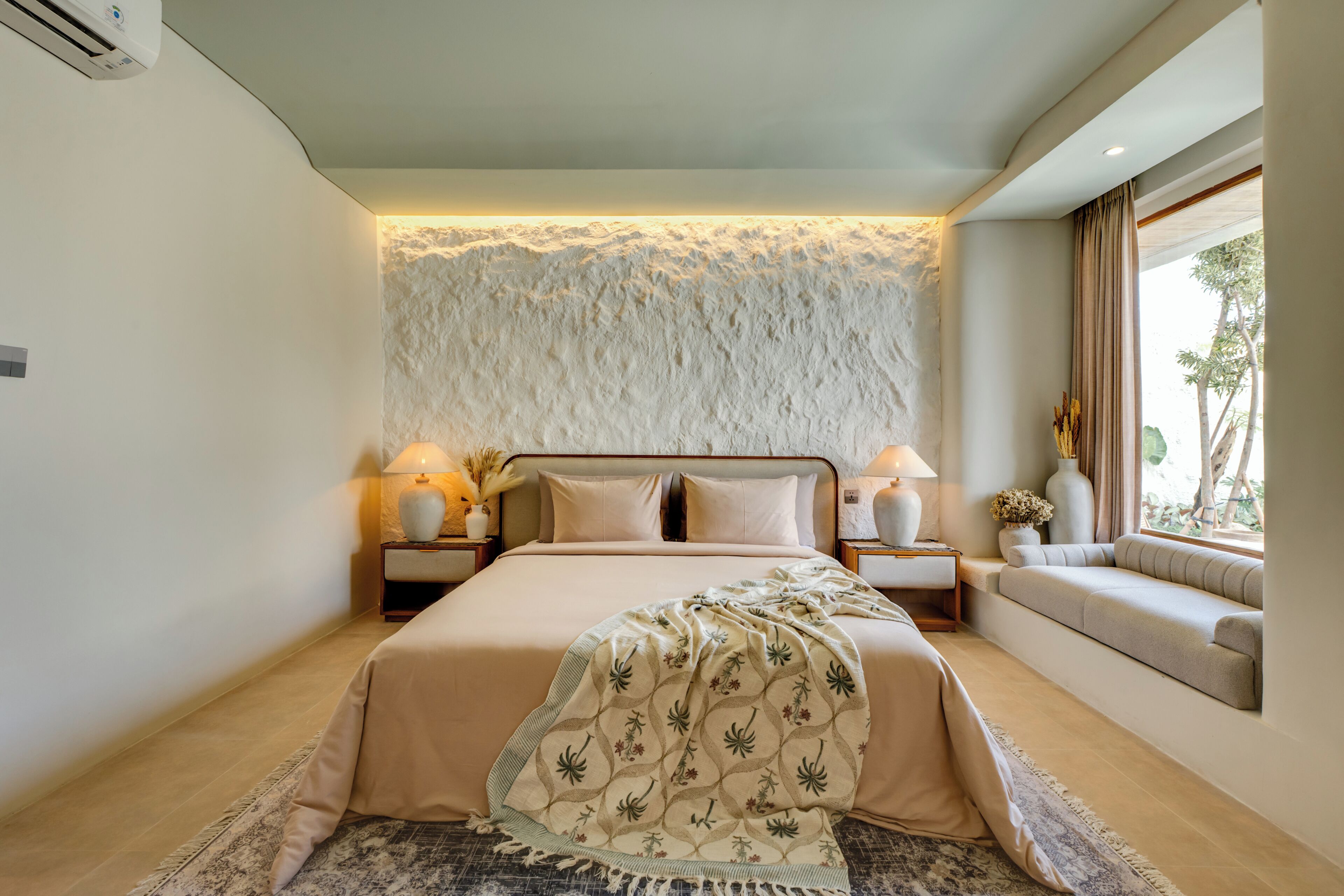 A modern bedroom with a large bed, bedside lamps, a decorative wall, and a window with a view.