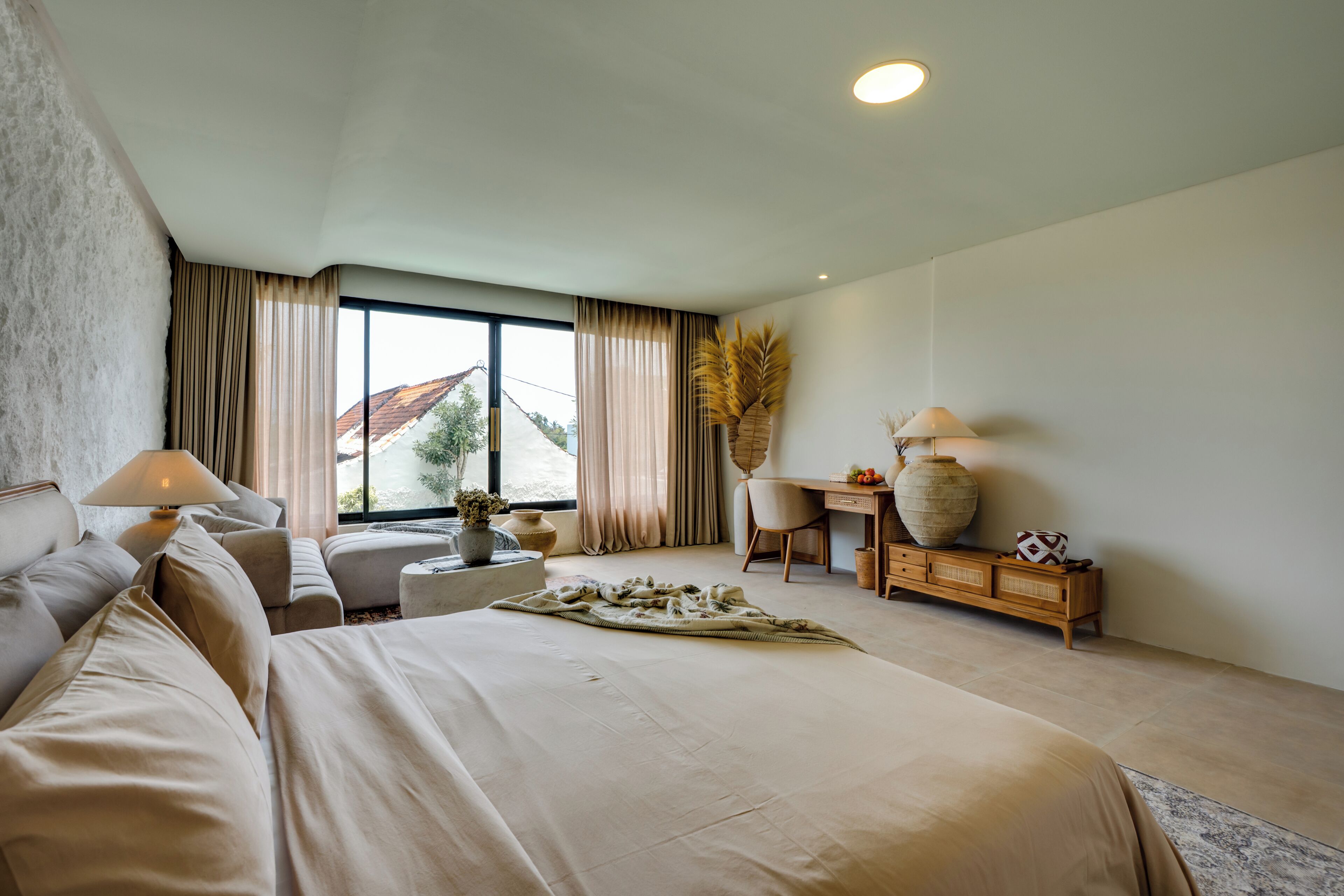 Ein modernes Hotelzimmer mit einem großen Bett, einem Schreibtisch, einem Sessel und Blick ins Freie.