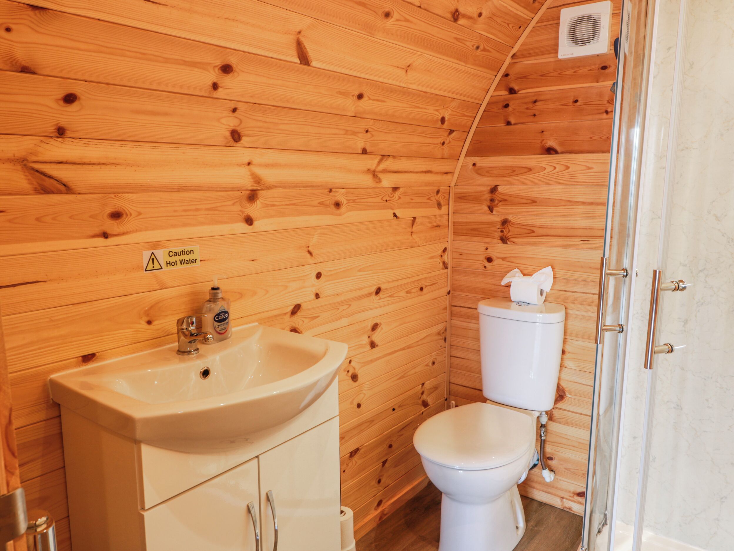 A wooden cabin bathroom with a sink, toilet, and shower.