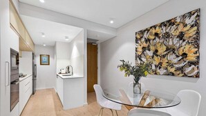 Eine moderne Küche mit weißen Schränken, einem Glastisch und einem großen abstrakten Gemälde an der Wand.