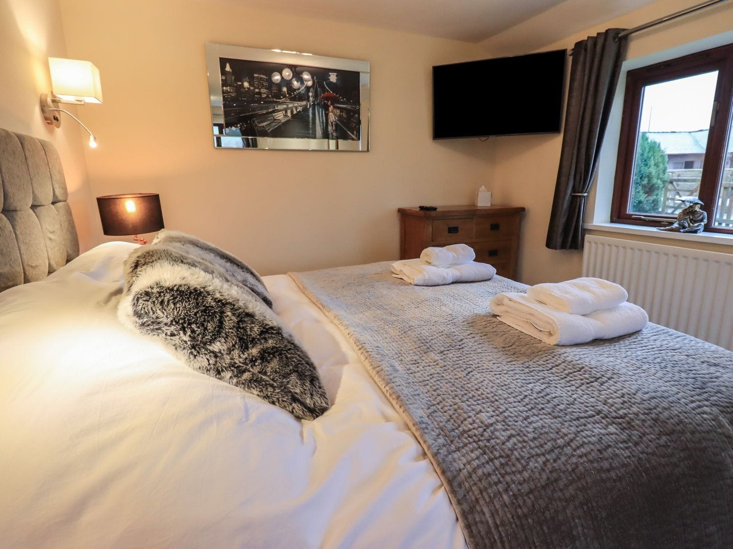 Una habitación de hotel con cama, televisión de pantalla plana, ventana con cortinas y un cuadro en la pared.