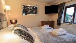 A hotel room with a bed, a flat-screen TV, a window with curtains, and a painting on the wall. - Orcaber Farm Retreat (Lancaster)