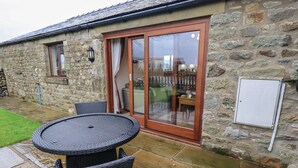 A stone building with a patio area featuring a round table and chairs, a sliding glass door, and a stone wall. - Orcaber Farm Retreat (Lancaster)