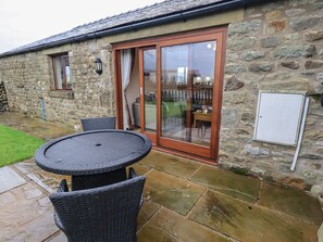 A stone building with a patio area featuring a round table and chairs, a sliding glass door, and a stone wall. - Orcaber Farm Retreat (Lancaster)