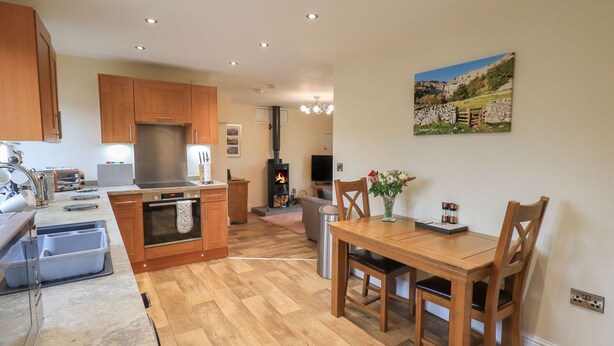 A modern kitchen with wooden cabinets, a built-in oven, and a dining area with a wooden table and chairs. - Orcaber Farm Retreat (Lancaster)