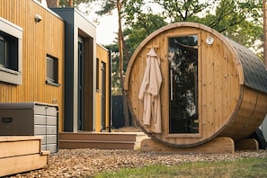 A wooden barrel-shaped structure with a door and a towel hanging on the inside. - Enjoy a romantic stay in the Forest Lodge with sauna for 2 people. A luxury villa in nature with a terrace, rain shower and comfortable box spring bed. (Lattrop-Breklenkamp)