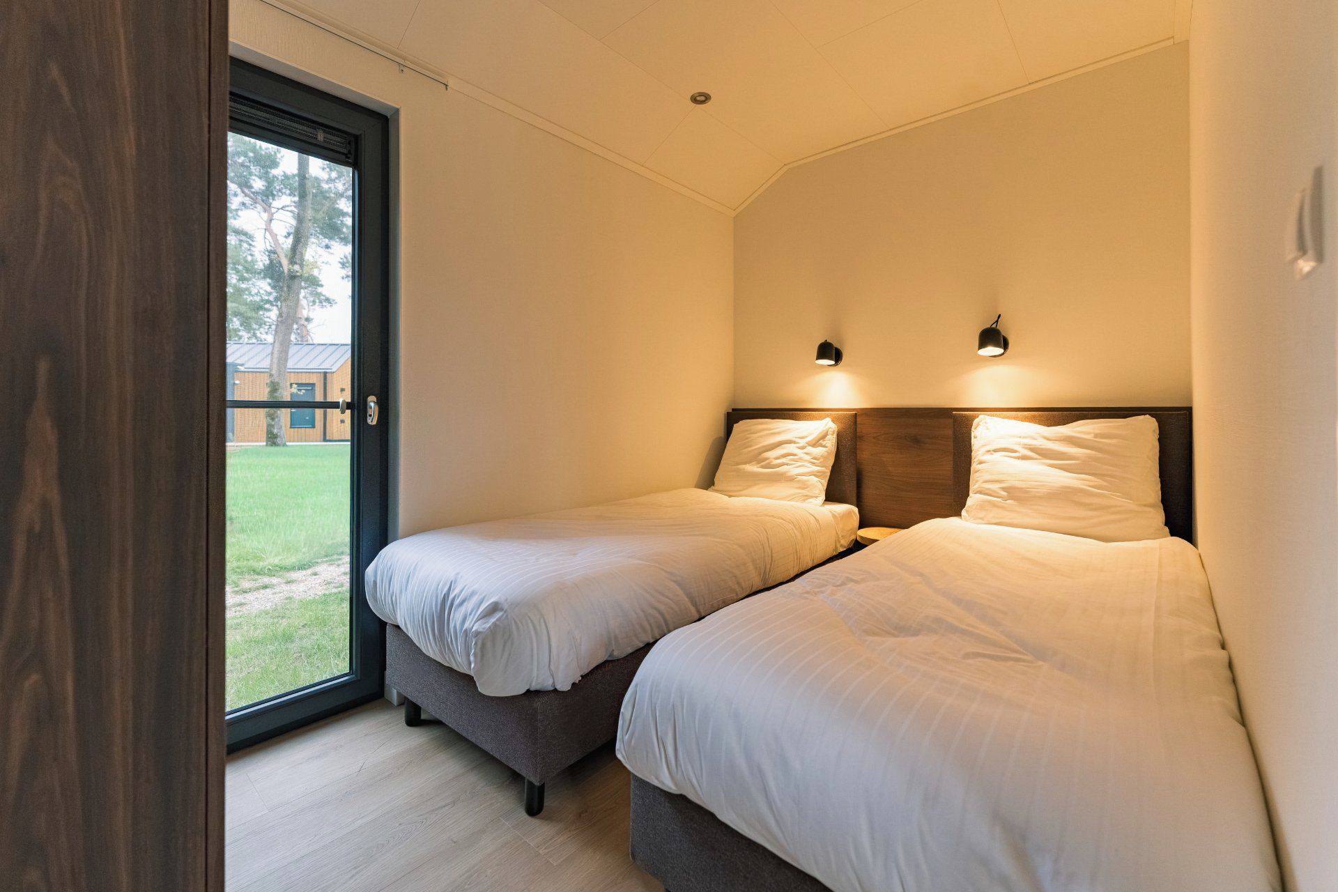Une chambre avec deux lits, une porte-fenêtre coulissante et une petite table de chevet.