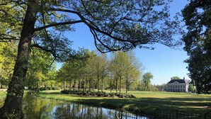 A serene park with a pond, trees, and a large building in the background. - Luxury Forest Lodge with hot tub and sauna for 2 people. Enjoy peace, nature and comfort with private wellness, a terrace and a modern kitchen. (Lattrop-Breklenkamp)