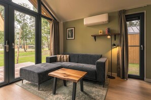 A modern living room with a sectional sofa, a wooden coffee table, and a large sliding glass door leading to an outdoor area. - Luxury Forest Lodge with hot tub and sauna for 2 people. Enjoy peace, nature and comfort with private wellness, a terrace and a modern kitchen. (Lattrop-Breklenkamp)