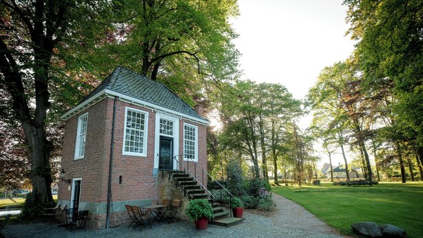A brick building with a staircase leading to a door, surrounded by trees and a paved area with outdoor furniture. - Luxury Forest Lodge with hot tub and sauna for 2 people. Enjoy peace, nature and comfort with private wellness, a terrace and a modern kitchen. (Lattrop-Breklenkamp)