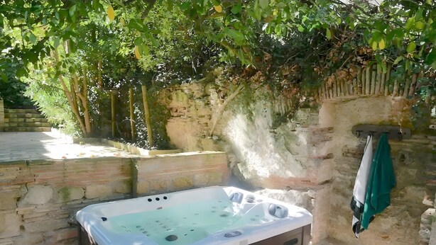 A hot tub in an outdoor setting with stone walls and greenery. - Gite VertCastel  – Charming Green Retreat with Pool and Spa (Castelnaudary)