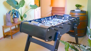 A room with a foosball table, a wooden bench, a potted plant, and a barrel. - Gite VertCastel – Charming Green Retreat with Pool and Spa (Castelnaudary)