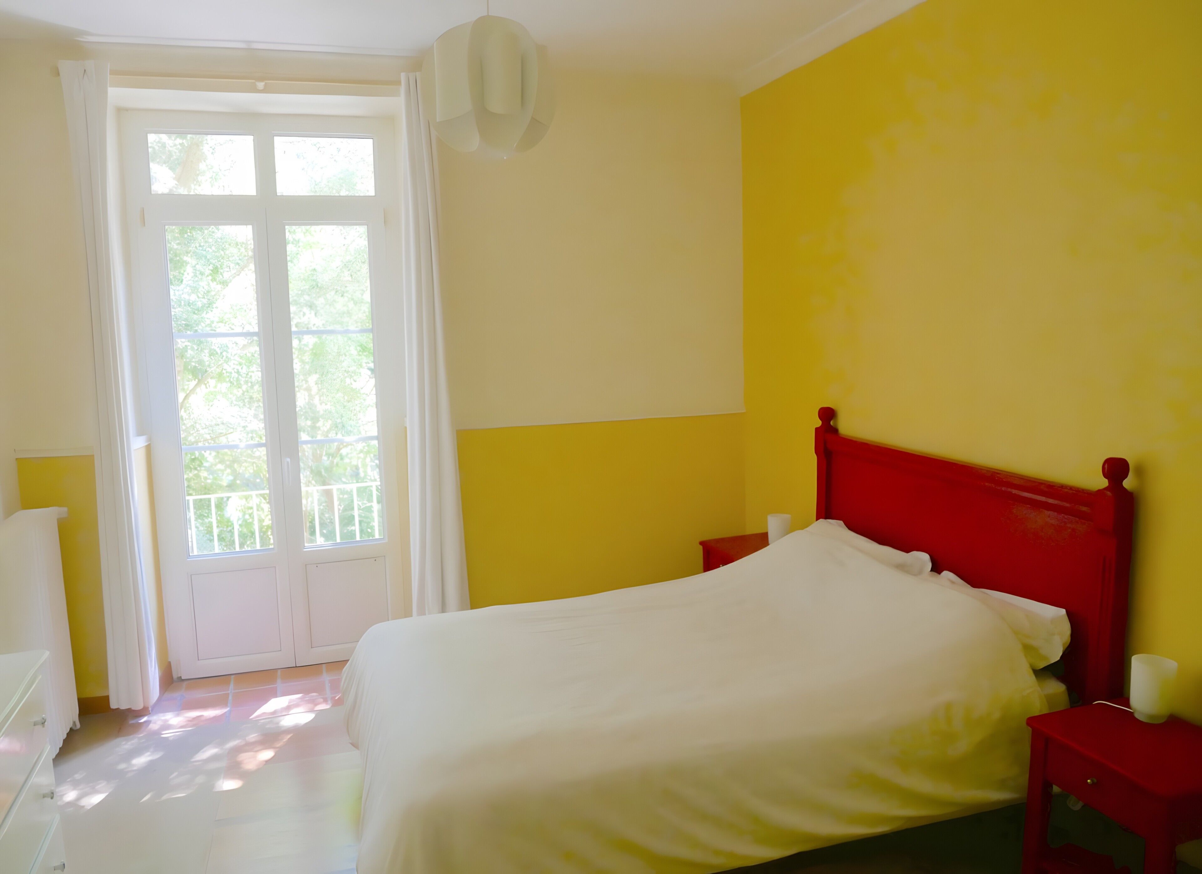 Ein Schlafzimmer mit einem Bett, einem Nachttisch, einem Fenster mit Vorhängen und einer Tür.