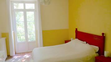 A bedroom with a bed, a nightstand, a window with curtains, and a door.