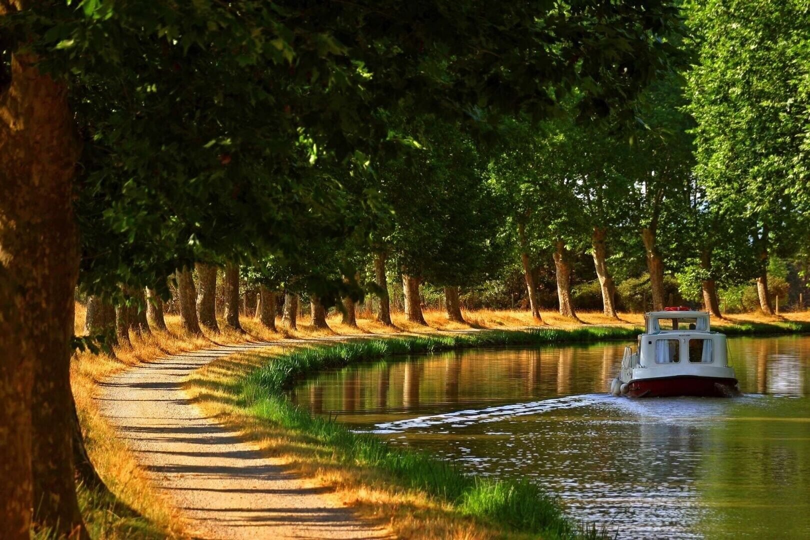 Un canal estret amb una embarcació, envoltat d'arbres i un camí.