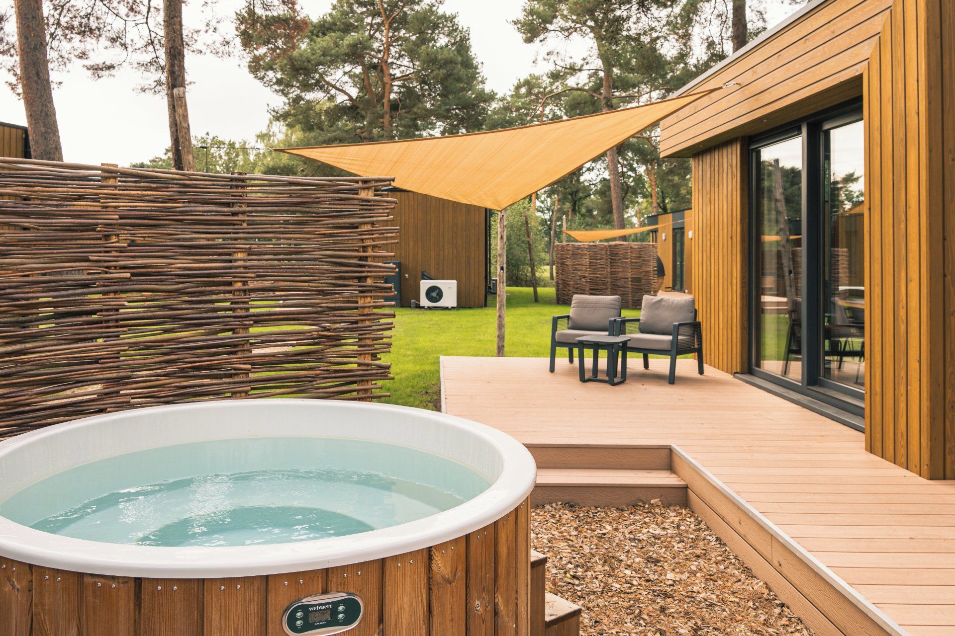 A wooden deck with a hot tub, outdoor furniture, and a large window overlooking a grassy area.