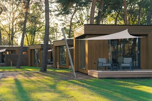 Eine moderne Holzhütte mit Terrasse und großen Fenstern, umgeben von Bäumen.