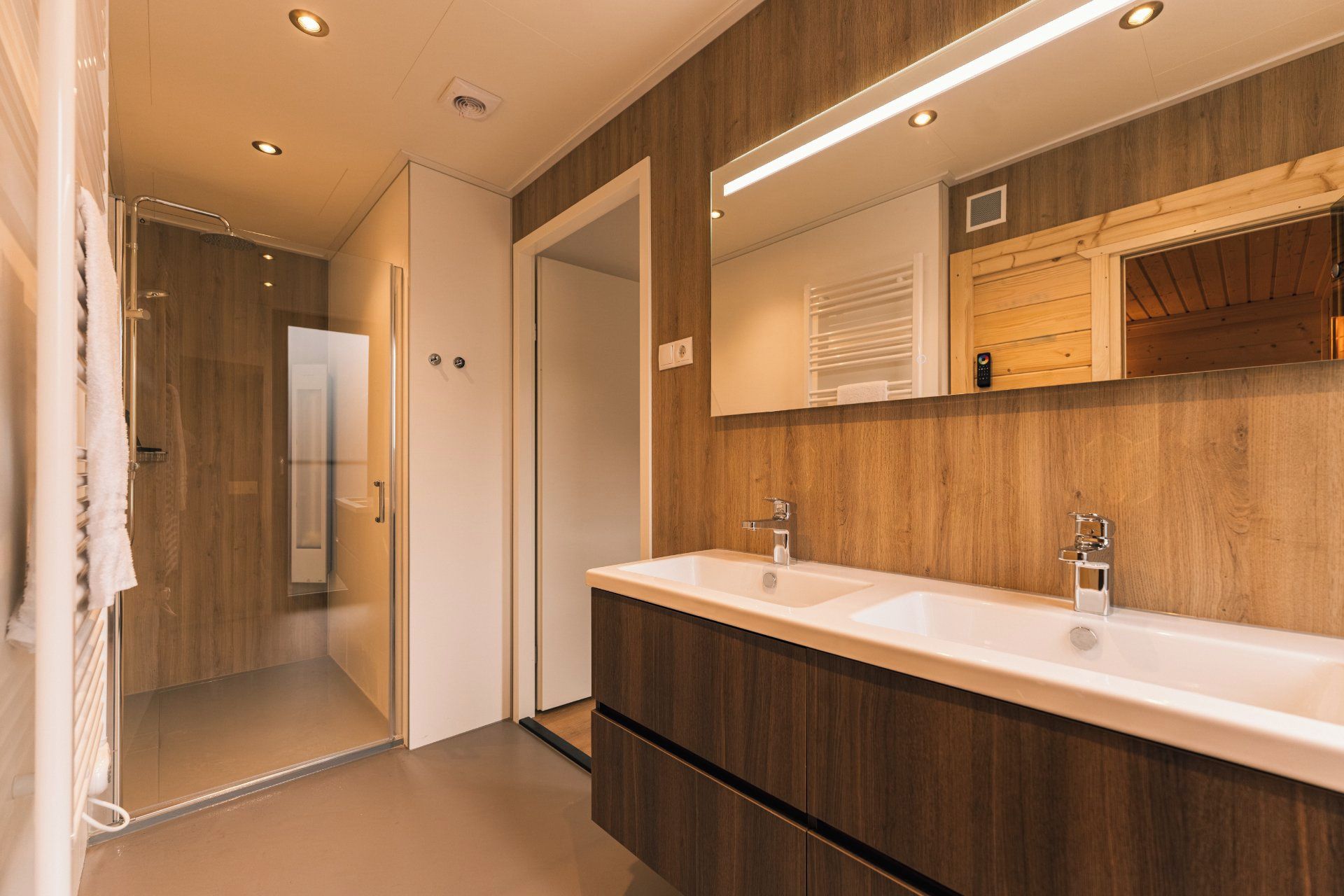 Ein modernes Badezimmer mit zwei Waschbecken, Holzvertäfelung und einer begehbaren Dusche.