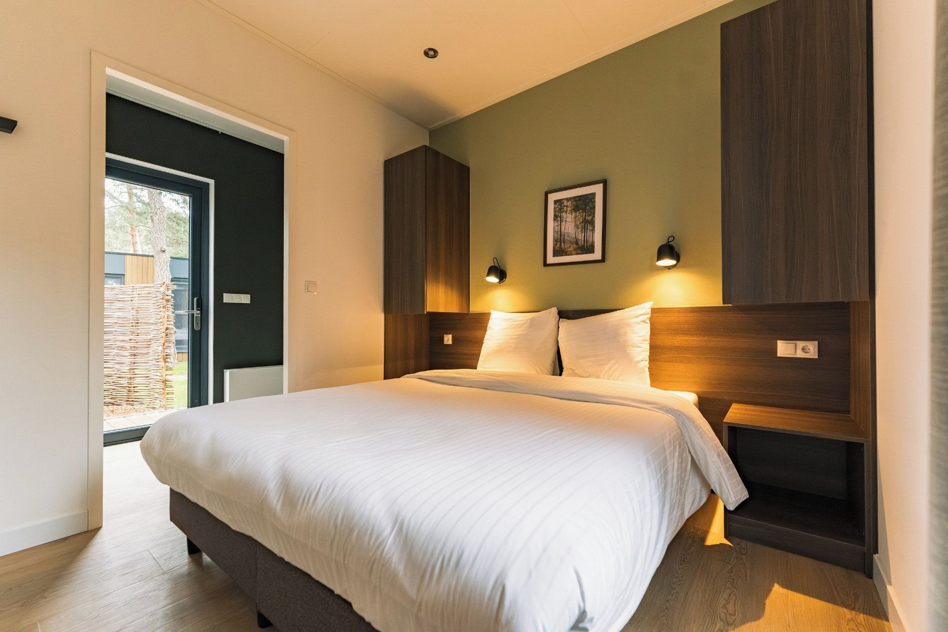 A bedroom with a large bed, wooden headboard, two bedside lamps, and a framed picture on the wall.