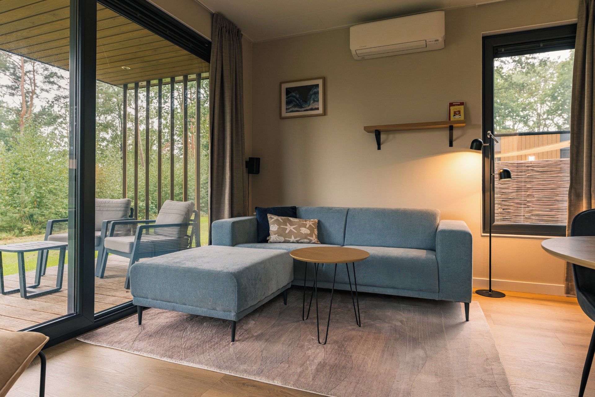 A modern living room with a blue sofa, a round coffee table, and a view of the outdoors through large glass doors.