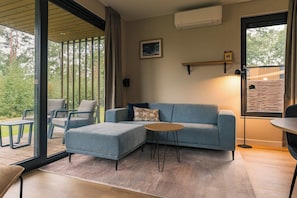 A modern living room with a blue sofa, a round coffee table, and a view of the outdoors through large glass doors.