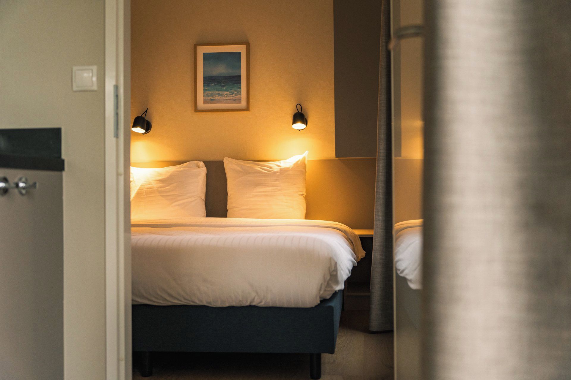A hotel room with a bed, two bedside lamps, and a framed picture on the wall.