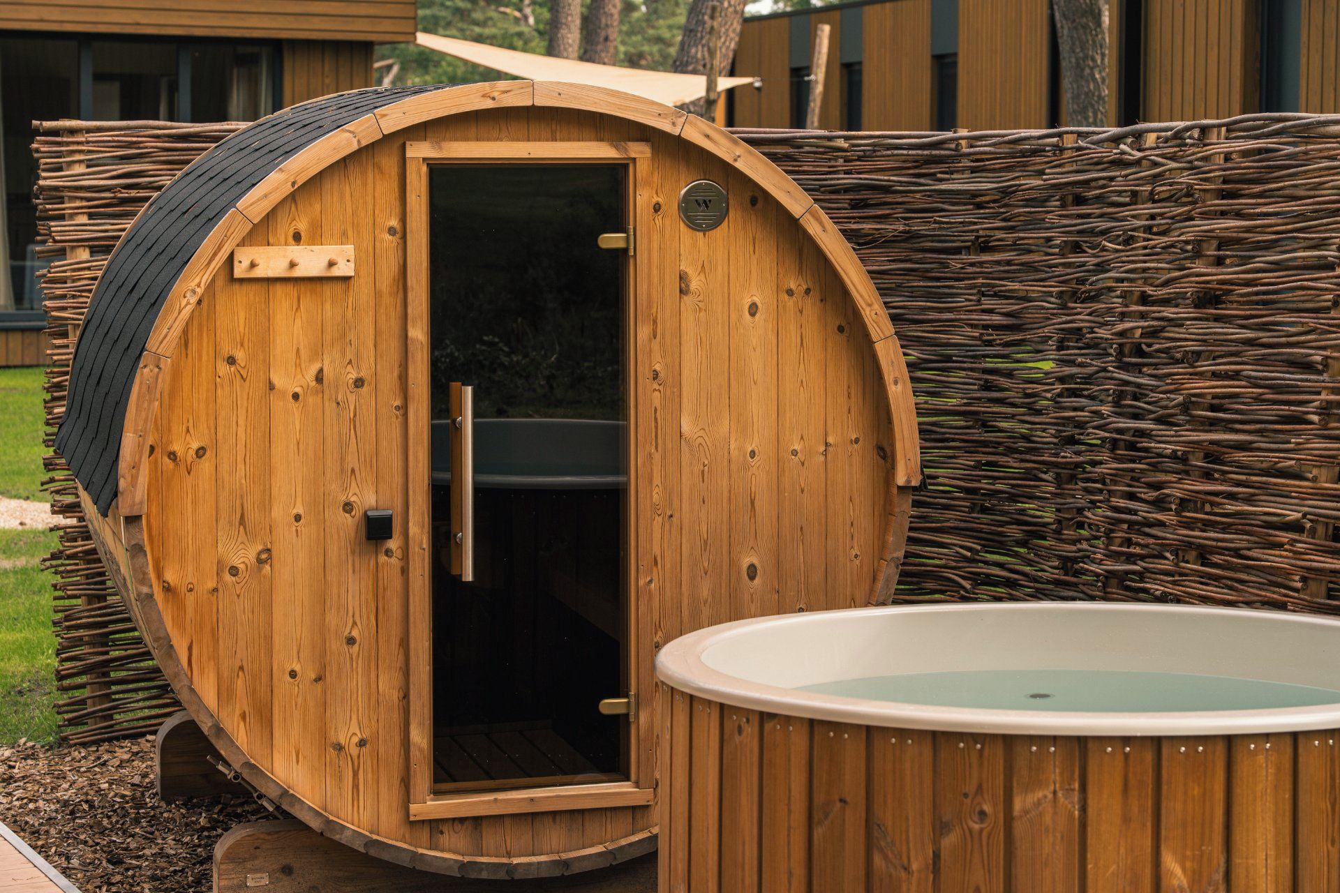 A wooden sauna with a door, a small window, and a hot tub in front.